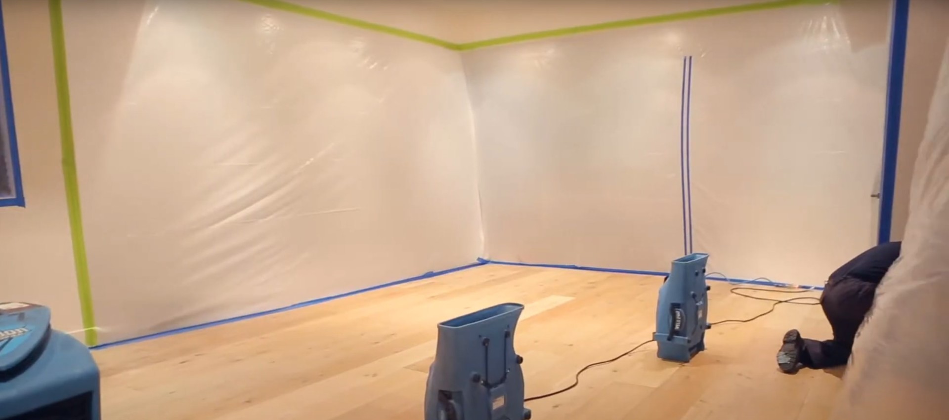 Professional water damage restoration room with multiple blue air movers and dehumidification equipment positioned on hardwood floor