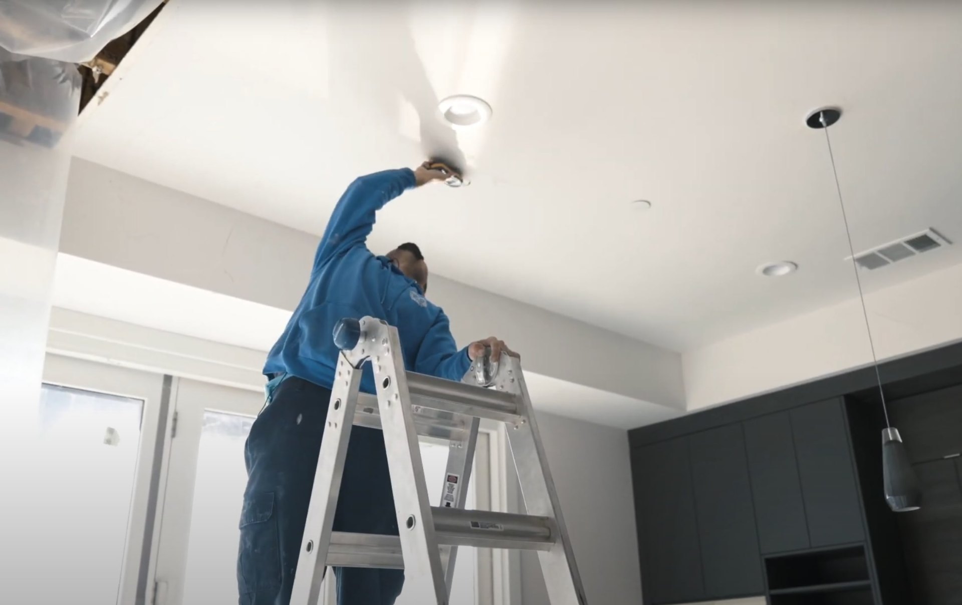 Water damage restoration technician on ladder performing ceiling repair and moisture remediation